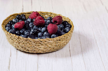 Fresh blueberries and raspberries with drops of water in a small wicker basket. Fresh fruit washed with water and ready to eat. Vegan food. Healthy food concept.の写真素材