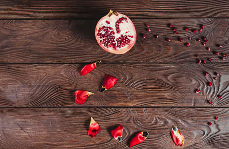 Top view of a pomegranate cut in half with its seeds scattered and flower petals forming a circle on a brown wooden table. Source of vitamins. Space for copying. Healthy food concept.の写真素材