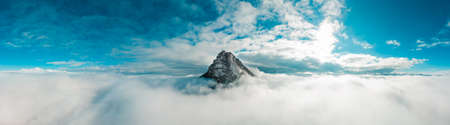 Panoramic aerial photograph taken with a drone. The peak of BeriÃ¡in, in the AndÃ­a mountain range, rises among the white clouds. In the background a deep blue sky and the sun rising through the clouds.の写真素材