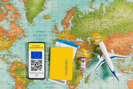 EU digital Covid certificate on the screen of a smart phone next to passport and airline tickets,...