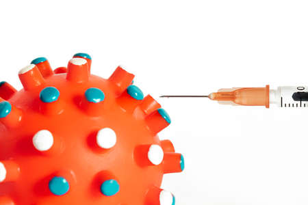 Detail of a syringe with vaccine about to be injected into the covid-19 coronavirus infection molecule in the form of a bulging orange rubber ball on a white background. Medical and health concept.の写真素材