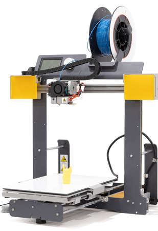 Close-up of a 3D printer and the yellow 3D printed plastic part on a white background. Concept of...