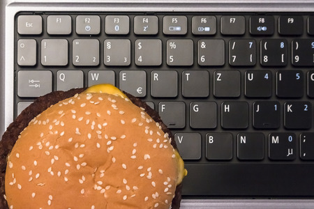 Cheeseburger on laptop keyboard - a fast food lunch in the Workplaceの写真素材