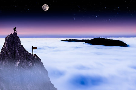 Hiker on Top of a Mountain Looking Over the Cloud Cover at Nightの写真素材