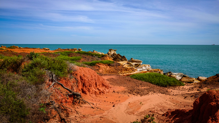 Red dirt coastline against ocean and cloudy blue skyの写真素材