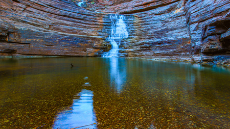 Waterfall flowing over rocky cliff into river with reflection in waterの写真素材