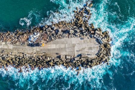 Aerial drone view of the Newcastle breakwall extending into the Pacific Ocean with waves moving along the rocky structure.