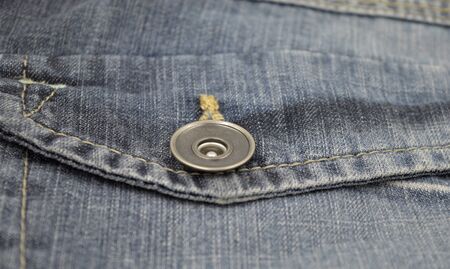 Metal closeup buttom on back pocket of blue faded jeans. 