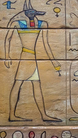 Egyptian god Anubis carved on stone wall with hieroglyphs.