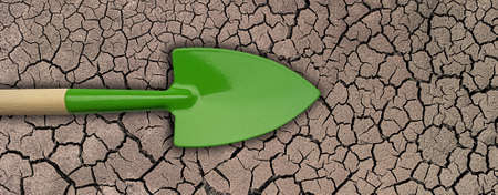 Green garden trowel on dry cracked soil.