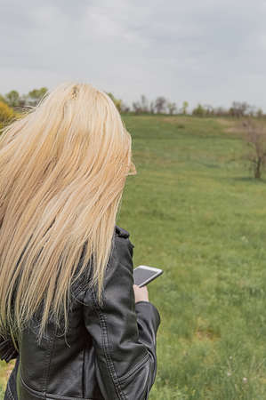 Blond young woman with phone in hand in green springtime field.の写真素材