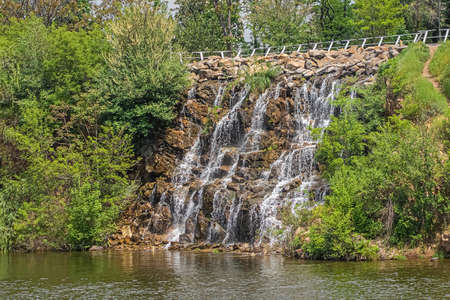 Waterfall above river between trees in sunny summer day.の写真素材