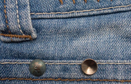Blue denim background with white and brown stitches and metal buttons.
