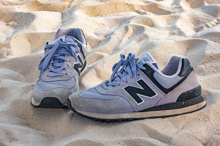 Dnipro, Ukraine - May 15, 2021: Pair of worn out purple New Balance sneakers on sand of beach.