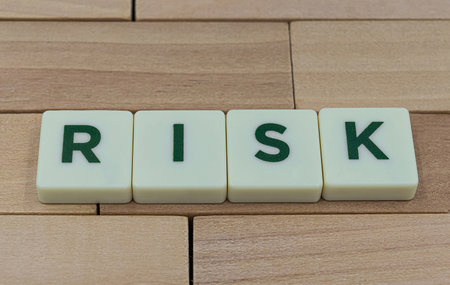 Plastic white cubes with sign RISK on wooden block background.