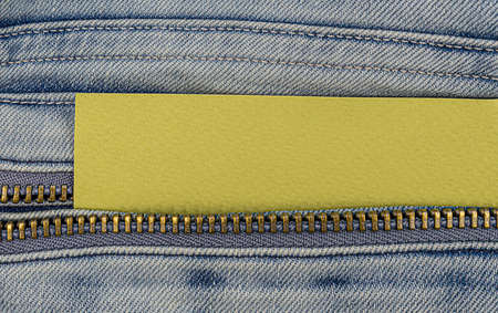 Metal open zipper and yellow paper blank on light blue jeans.