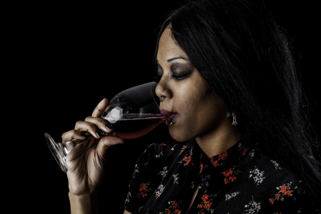A sexy gothic african american drinking red wine from a glass against a dark background. の写真素材