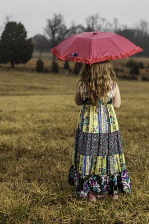 young girl holding an umbrella in the rain looking out at a fieldの写真素材