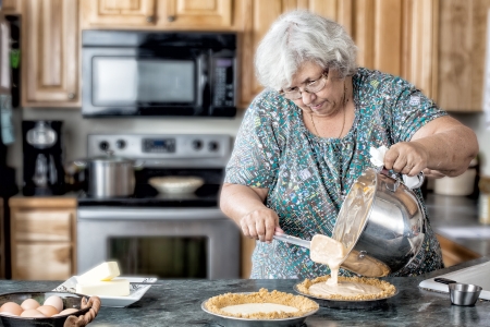 Photo of a grandmother elderly active woman in a natural kitchen filling pies. White older woman in the kitchen baking. の写真素材