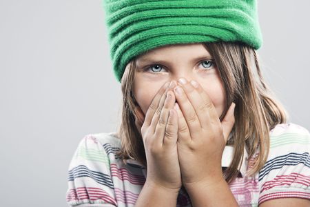 Shot of a Cute Child with Green Hat Covering her Mouth and Noseの写真素材