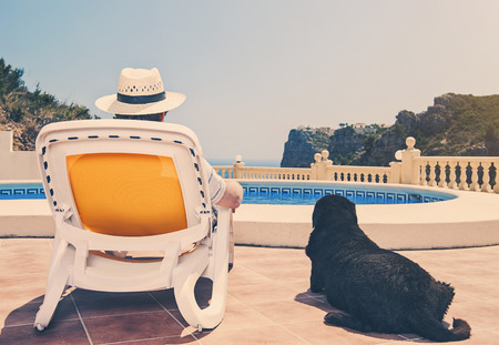 Owner relaxing by pool with dog beside him