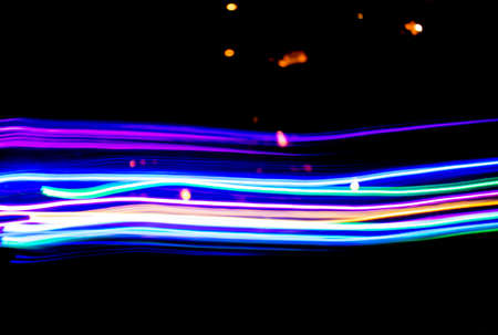 Neon color light tracks against night sky with bokeh lights