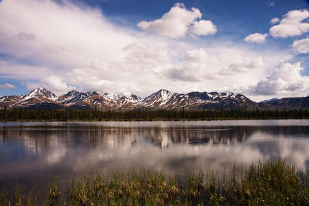 Jagged snowy mountain peaks with snow on the top reflected in shallow river during early summer.の写真素材