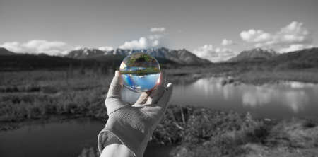 Hand holding a crystal ball to reflect beaver dam, pond, mountains, and reflectionの写真素材