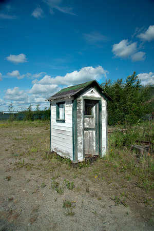 Small white and green painted shed in Alaska, with trees and blue skies in background.の写真素材