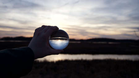 Reflection of cloudy dark sunset in crystal ball held by handの写真素材