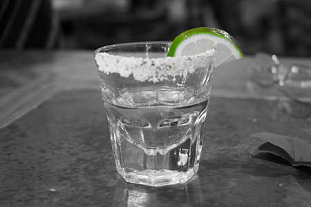 Black and white photo of tequila shot glass with salt on the rim and wedge of lime. Green was the...
