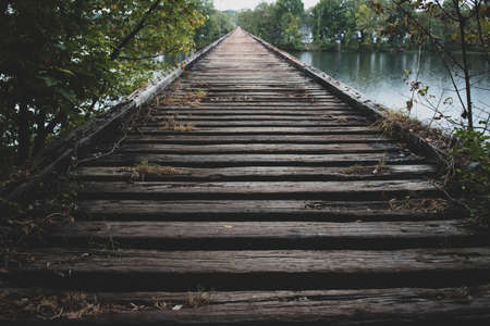 Old wooden bridge once part of railroad track, crossing a river with forest on both sides.の写真素材