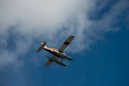 A small airplane with pontoons flying above with blue sky and clouds on a sunny summer day in...