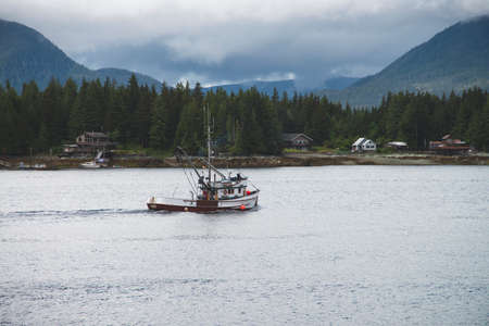 Fishing boat in the water with misty mountains and forest during an Alaska summer.