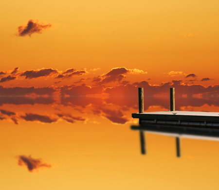 Orange sky with red clouds reflecting back on its self.  With wood boat peirの写真素材