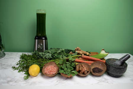 Healthy fresh vegetables, spices, and herbs on white and grey marble with blender and reusable plastic cupの写真素材