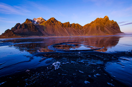 Jagged Vestrahorn Mountain in Iceland, with reflection in frozen sand and wagon wheel.