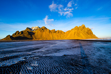Frozen saltwater over the black sandy beach, with Iceland's Vestrahorn in the background.