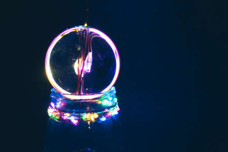 Neon color light trails reflected in crystal, lens ball with blue background.