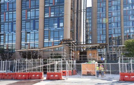 High-rise buildings under construction, with marked-off sidewalks, dumpsters, and workers.