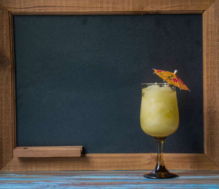 Cocktail drink in front of chalkboard for drink menu, with tropical wood table