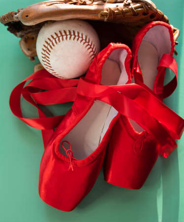 Bright red ballet pointe shoes, grouped with softball and mitt.  Against a teal or green background.の写真素材
