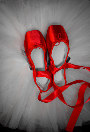 Red ballet pointe shoes set on top of a white tutu.