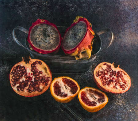 Tropical fruit sliced in half displayed against a dark background and galvanized bucket. Edited to look like an ink image.の写真素材
