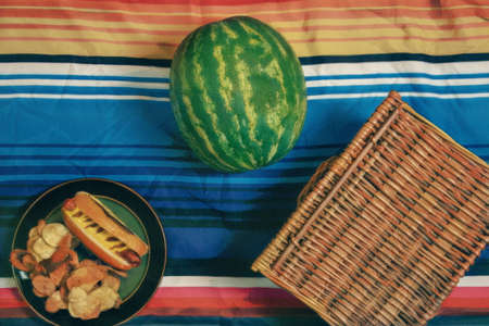Watermelon, chips and a wicker basket on a striped background
