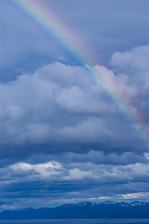 Rainbow in the blue sky with white clouds and mountains in the backgroundの写真素材