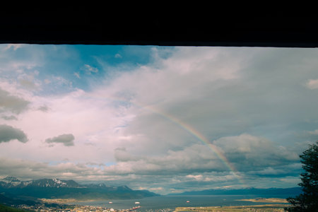 View of the Mountains surrounding the city of Ushuaia.  With a rainbow arching over the city on a summer day.の写真素材