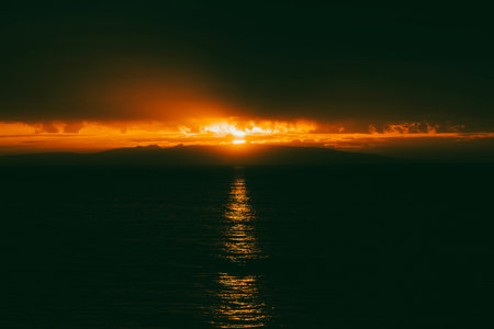 Sunset over the Beagle Channel in Argentina.  Image Has a sliver of sunlight due to the storm clouds, and there is a faint silhouette of land.の写真素材