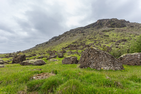 Green mountain slope on Iceland covered by grass with big rocks in foreground. Arctic nature in summer. Green fresh icelandic landscape.の写真素材