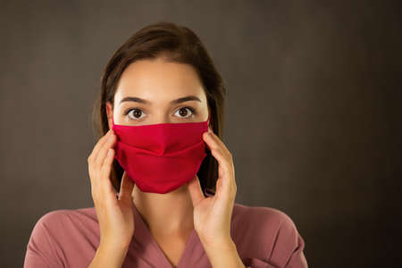 Frightened woman touching her pink face mask with fingers. Concept of fear from respiratory illness spreading between humans. Protective breathing filter against coronavirus infection.の写真素材